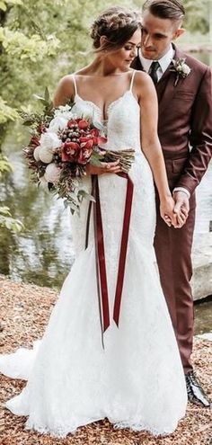 a bride and groom standing next to each other in front of a pond holding hands