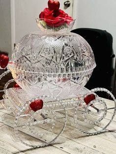 a glass carriage with two roses on it's top sitting on a wooden table