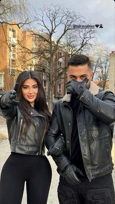 two people standing next to each other wearing leather jackets and black leggings, posing for the camera