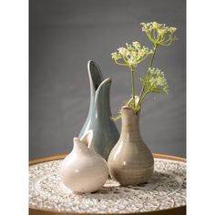 three ceramic vases with flowers in them on a lace doily tableclothed tray