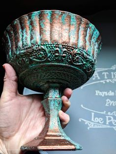 a close up of a person's hand holding a green and brown cup with designs on it