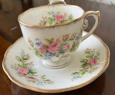 a tea cup and saucer on a wooden table with flowers painted on the side