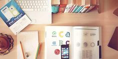 an open book sitting on top of a wooden desk next to a laptop and phone