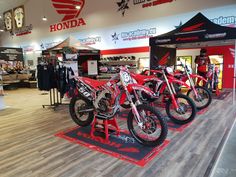 three dirt bikes are on display in a store with wooden flooring and red accents