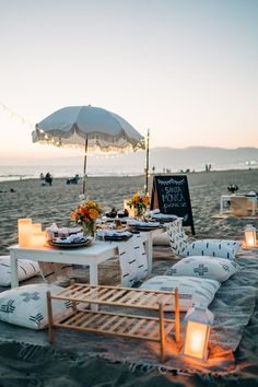 a table set up on the beach for an outdoor dinner party with candles and food