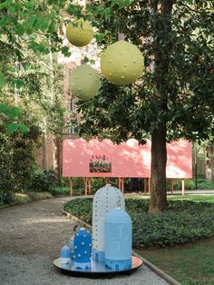 an outdoor sculpture in the middle of a park surrounded by trees and bushes with balls hanging from them