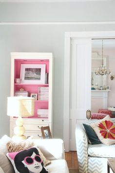 a living room filled with furniture and a pink book shelf in the corner next to a white door