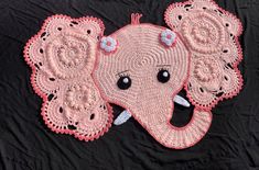 crocheted pink elephant with blue flowers on it's head laying on a black blanket