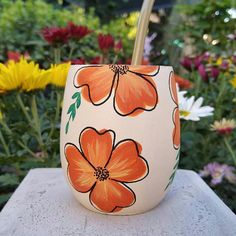 an orange flower painted on the side of a white cup sitting on top of a table