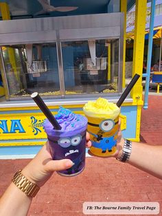 two people holding up drinks in front of a building with a yellow and blue sign