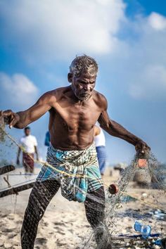 a man standing on top of a sandy beach holding a fishing net with his hands