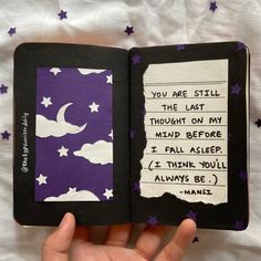 a hand holding an open book with writing on the pages and stars in the background