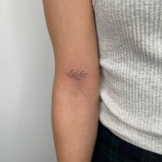 a woman's arm with a small leaf tattoo on the left side of her arm