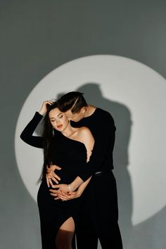 two women are hugging in front of a white circle with the shadow of an object behind them