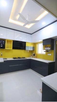 an empty kitchen with yellow and gray cabinets, white counter tops and ceiling fan in the center