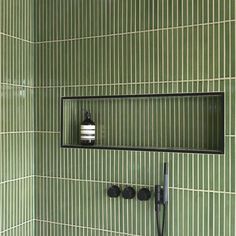 a green tiled bathroom with a shower head and soap dispenser on the wall