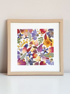 an art print with colorful flowers in a wooden frame on a white table next to a wall