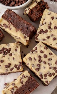 chocolate chip brownies cut into squares on top of parchment paper with a bowl of chocolate chips in the background