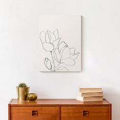 a wooden dresser with two books and a plant on top of it next to a white wall