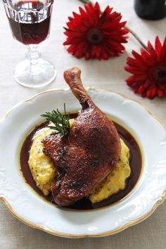 a piece of meat and mashed potatoes on a white plate with red flowers in the background