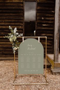 a sign that is sitting in front of a wooden building with flowers on the side