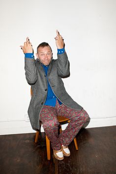 a man sitting on top of a wooden chair holding his hands up in the air