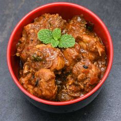 a red bowl filled with meat and garnish on top of a black table