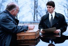 two men sitting at a table talking to each other in front of a suit case