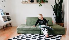 a little boy sitting on top of a green couch in front of a potted plant