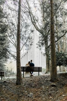 two people are sitting on a bench in front of a large white building surrounded by trees