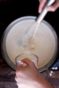 a person stirring something in a pot with a spoon and a glass next to it