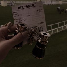 a person holding two binoculars in front of a horse race track with people on the sidelines