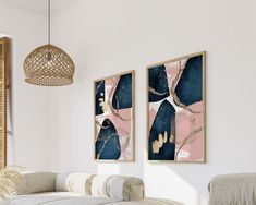 two paintings hang on the wall above a couch in a living room with white walls