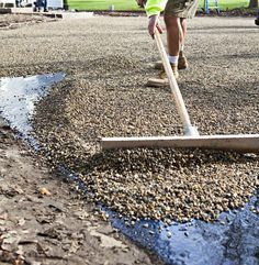 a man shoveling gravel with a long wooden stick in the middle of a parking lot