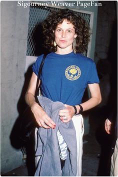 a woman with curly hair wearing a blue t - shirt and holding a gray bag