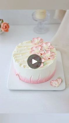 a white cake with pink flowers on it sitting on top of a table next to a vase