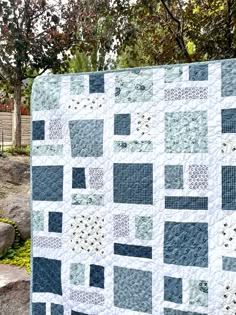 a blue and white quilt is hanging on a tree branch in front of some rocks