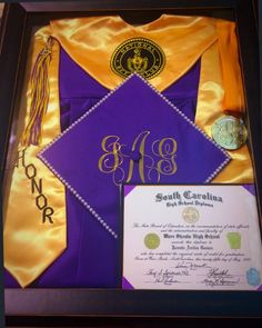 a purple and yellow graduation gown in a black frame with an award plaque on it