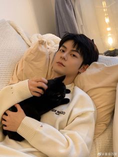 a person laying in bed with a cat on their chest and wearing a white sweater