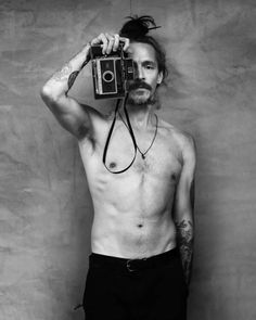 a shirtless man is holding an old camera up to his face while standing in front of a wall