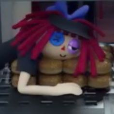 an animated doll with red hair and blue eyes sitting in front of some donuts