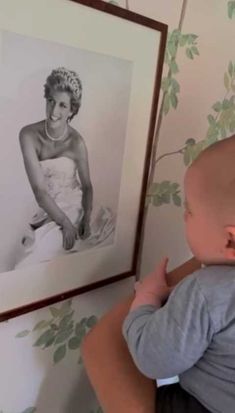 a woman holding a baby in her arms next to a wall with pictures on it