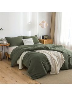 a bed with green sheets and pillows in a white room next to a wooden floor