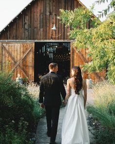 a bride and groom walking towards the barn