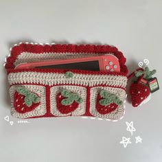 a crocheted purse with strawberries and a cell phone in the front, sitting on a table