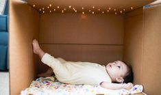 a baby laying in a cardboard box on top of a blanket and looking up at the ceiling