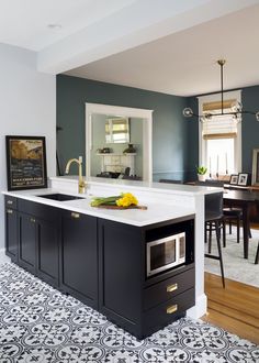 a kitchen with black cabinets and white counter tops, an island in front of a dining room table