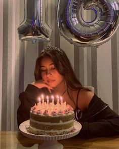 a woman sitting in front of a cake with lit candles on it and balloons behind her