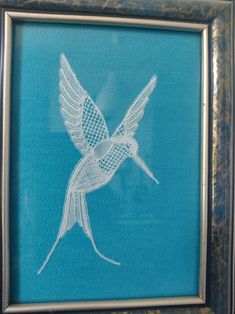 a white embroidered hummingbird in a blue frame