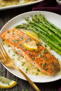 salmon and asparagus on a white plate with lemon wedged utensils